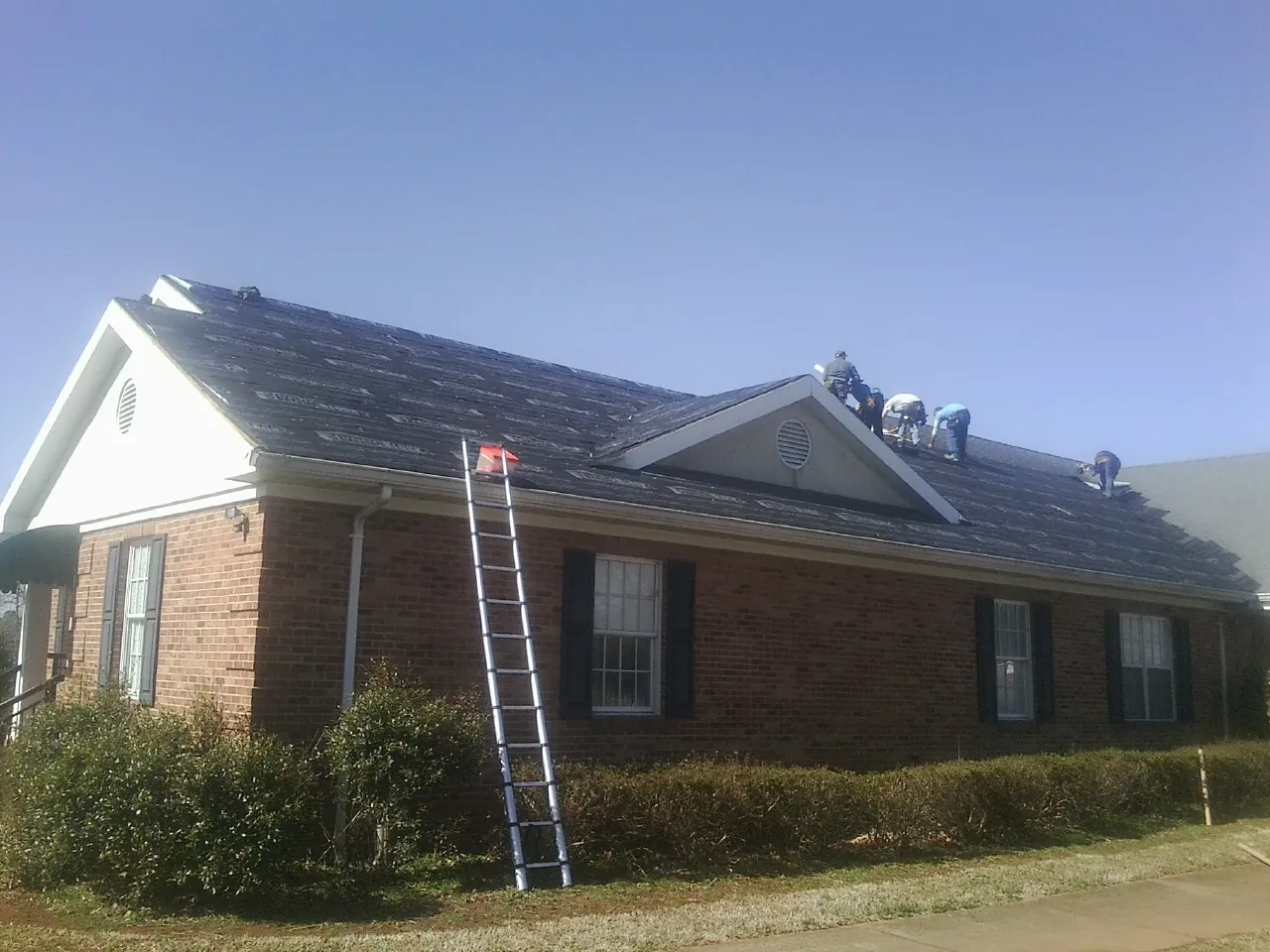 Crew tearing shingles off a brick ranch roof with a ladder set — Metal Roof Repair work by our crew in Jarrettsville