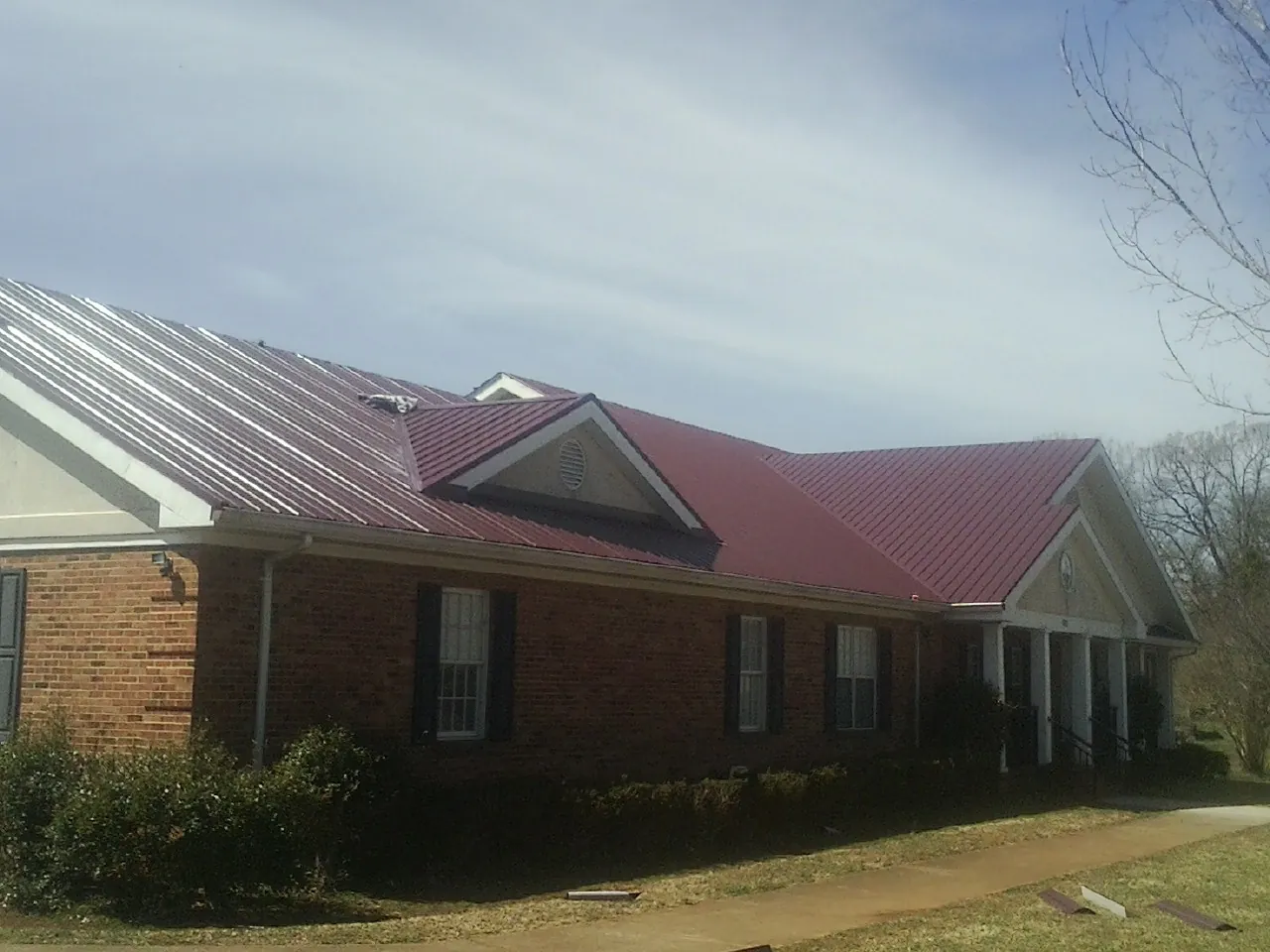 Red metal roof with gabled entries on a long brick building, from a Hail Damage Roof Repair job in Jarrettsville