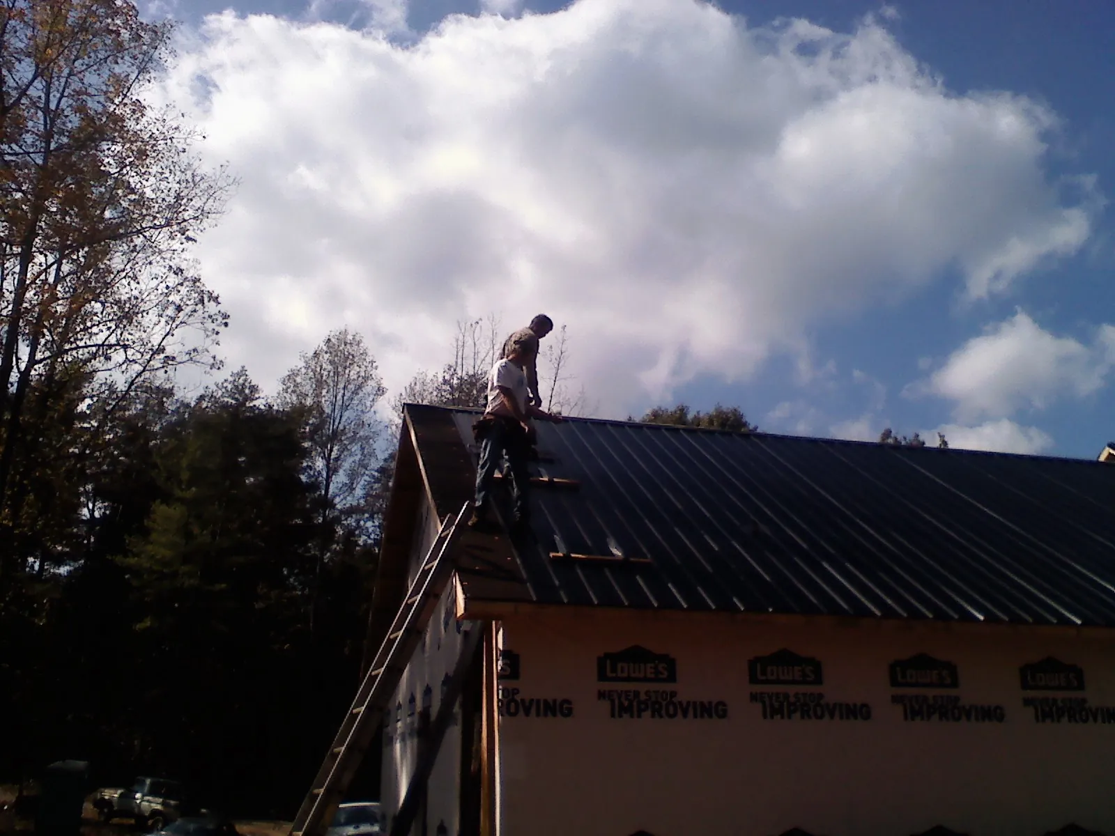 Roofer fastening dark metal panels high against a cloudy sky, from a Roof Inspection job in Jarrettsville