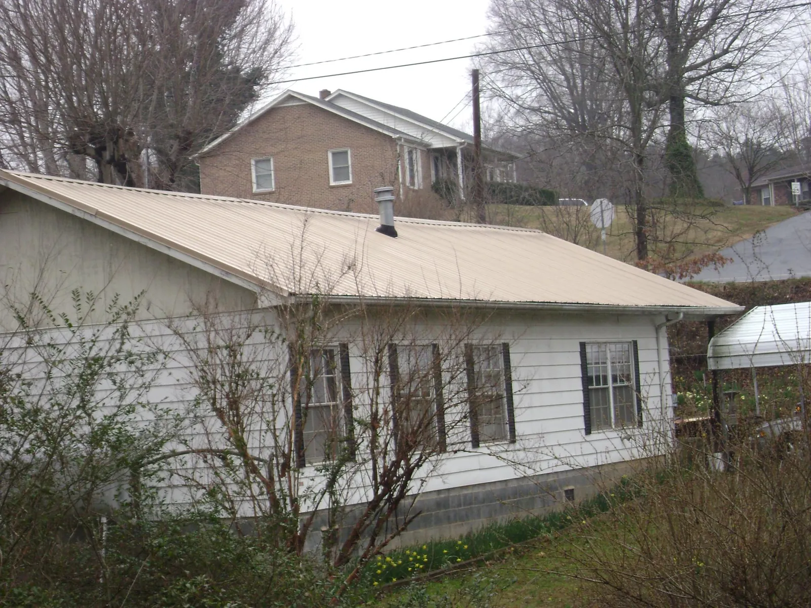 Tan metal roof on a white sided house set into a hillside — Commercial Roofing by Roofing Brothers in Jarrettsville